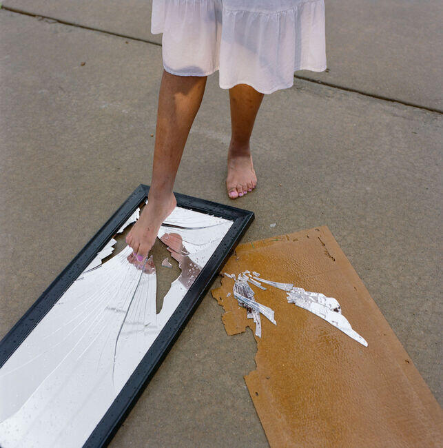 Jayanne, 14, steps into a broken mirror.USA. Missouri. St. Louis. May 2025. Jayanne (14) steps into a broken mirror.